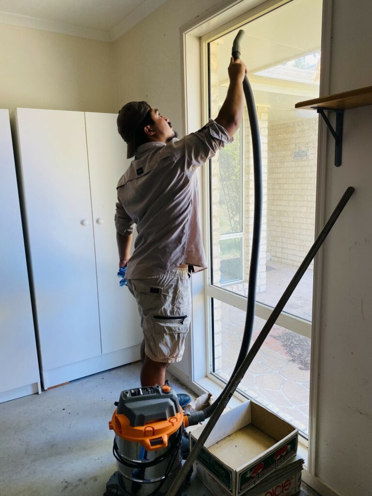 man vacuuming the inside of a window frame